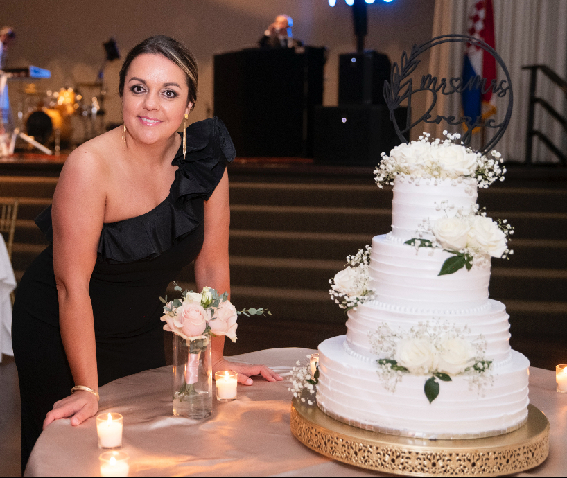 Lela standing beside a tiered white wedding cake decorated with flowers